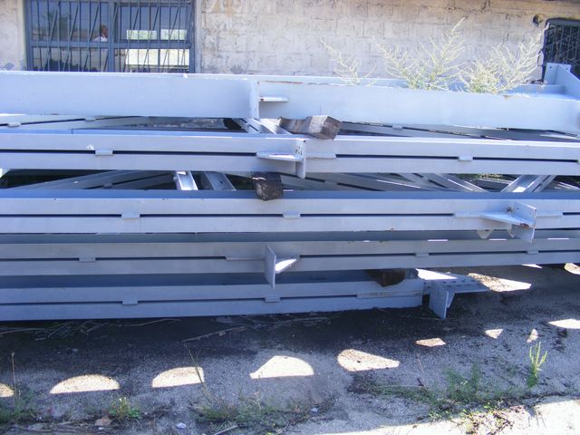 Stivă de tronsoane metalice cu zăbrele depozitate în aer liber